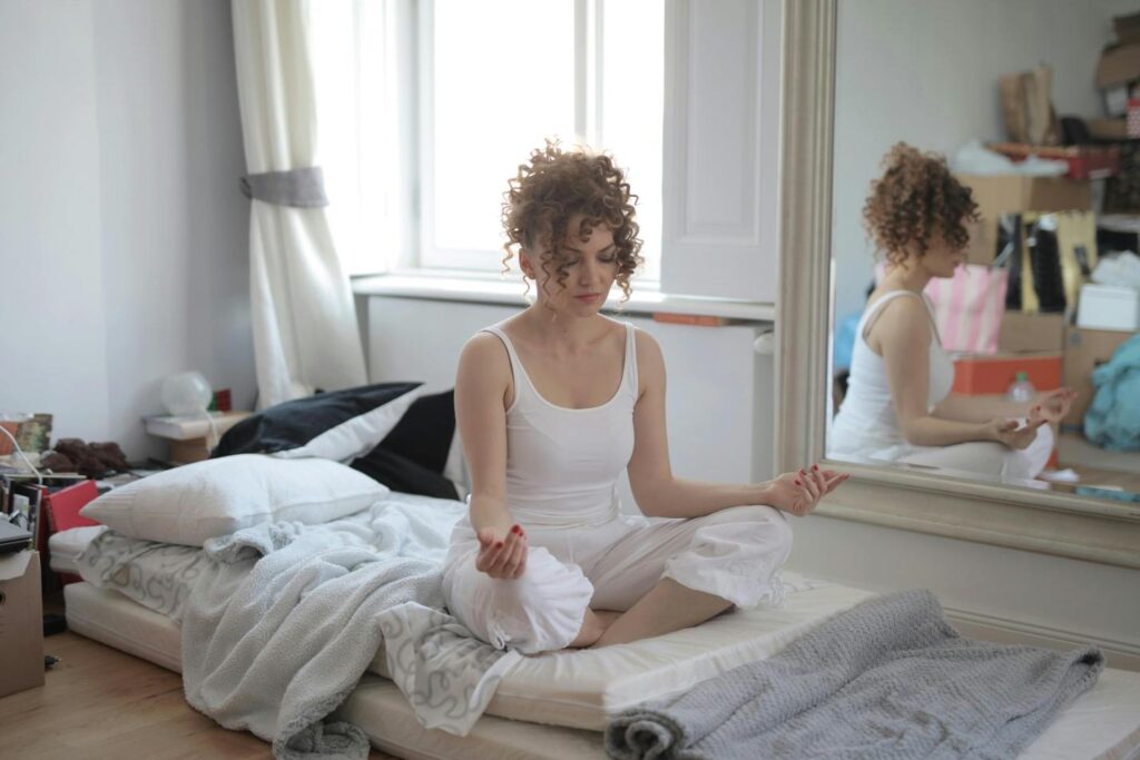 Woman meditating on a mattress on the floor reducing stress during the moving process